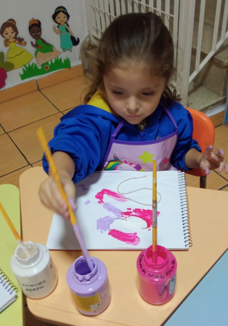 Criança pintando com pincel e tinta guache na aula de artes