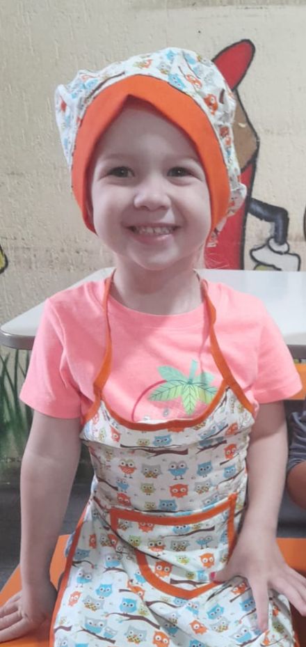 Criança sorrindo com touca e avental de chef na aula de culinária